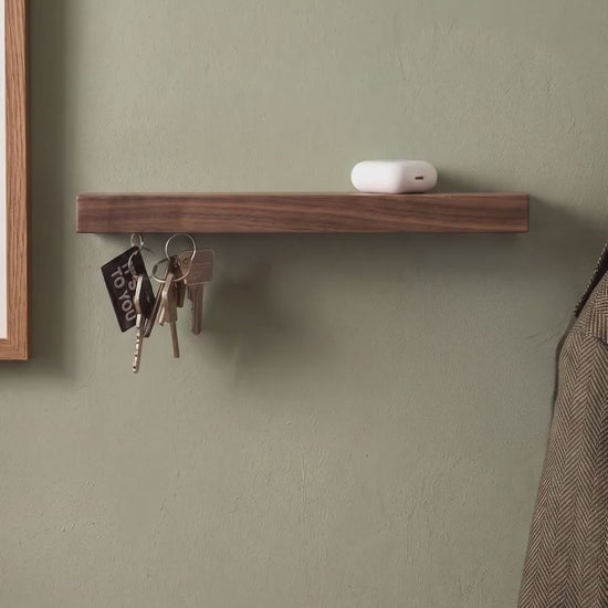 Een hand hangt sleutels aan de magnetische HangKey Plankie XL van notenhout tegen een groene muur.